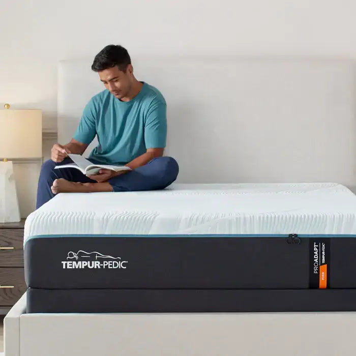 Man reading a book on the Tempur-Pedic ProAdapt Firm 12" Mattress in a modern bedroom setting.
