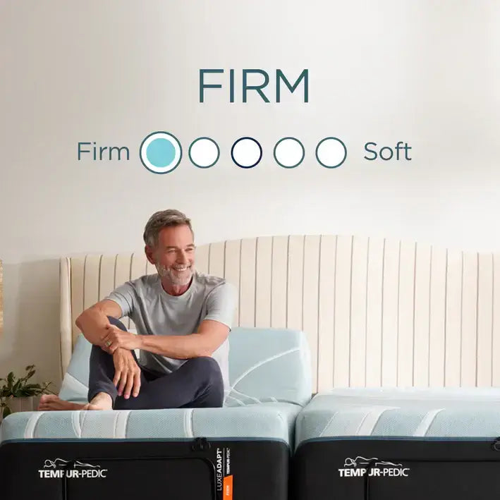 Man sitting on a Tempur-Pedic mattress, indicating firmness level with "FIRM" on the wall behind him.