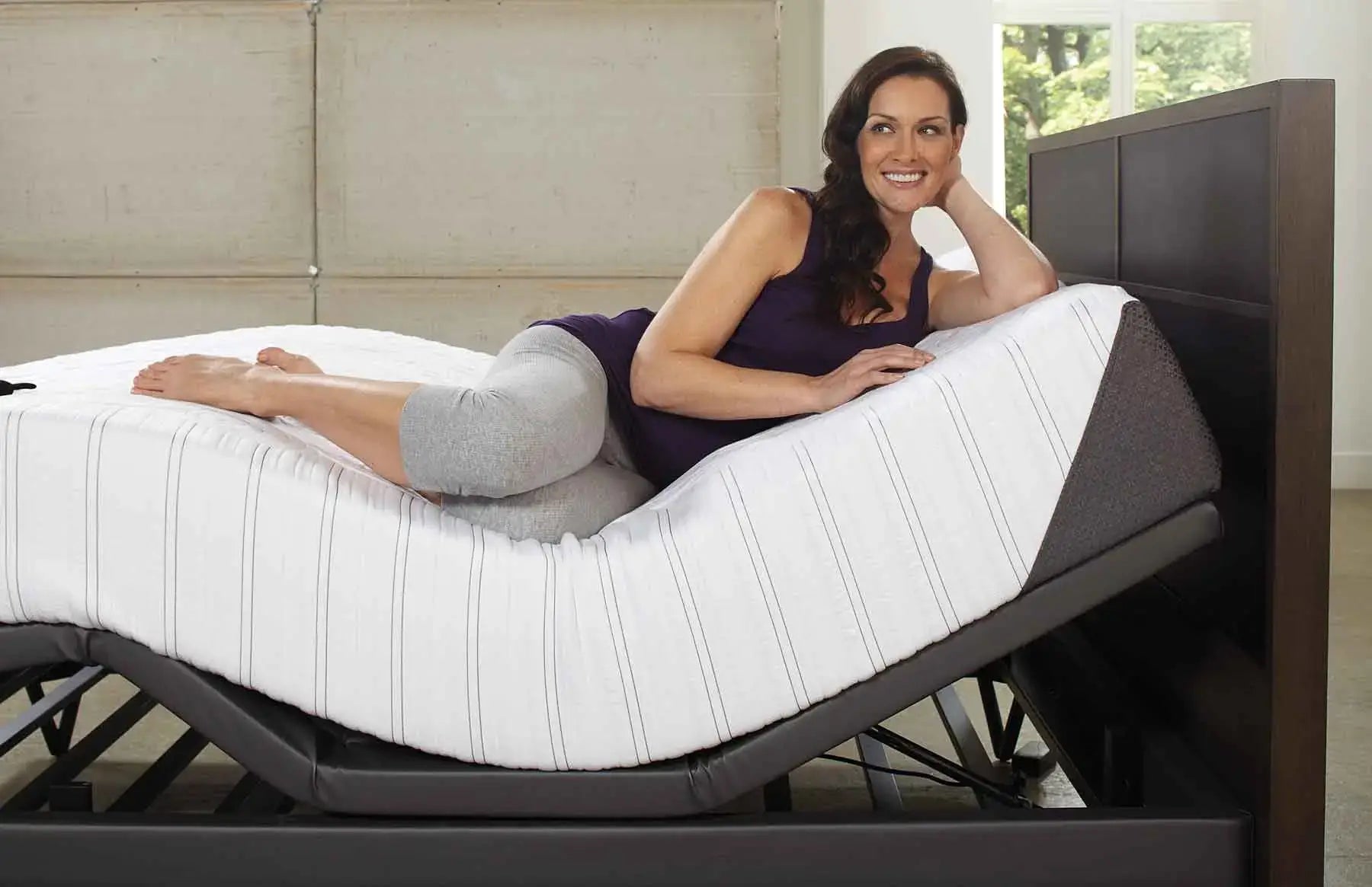 Woman relaxing on an adjustable bed, showcasing comfort and flexibility in modern bedding solutions.