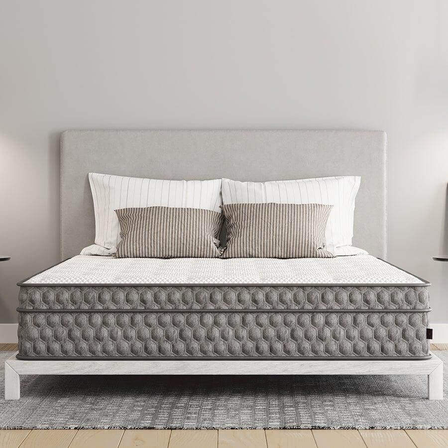 Modern grey mattress on a stylish bed frame with striped pillows in a cozy bedroom setting.
