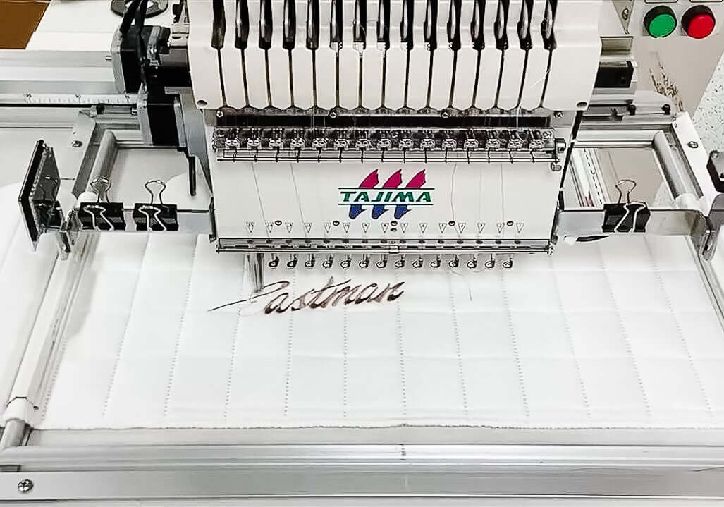 Tajima embroidery machine creating custom text on fabric, showcasing advanced stitching technology and craftsmanship.