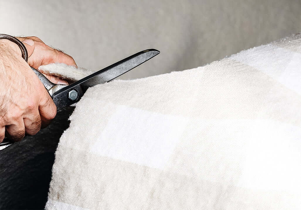 Person cutting a soft white plaid fabric with scissors, showcasing textile craft and DIY skills.