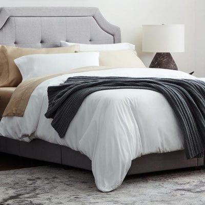 Cozy bedroom with a gray upholstered bed, neutral bedding, and a stylish lamp on a nightstand.