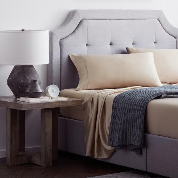 Elegant bedroom setup featuring a gray upholstered headboard, cream pillows, and a cozy throw blanket on a stylish bed.