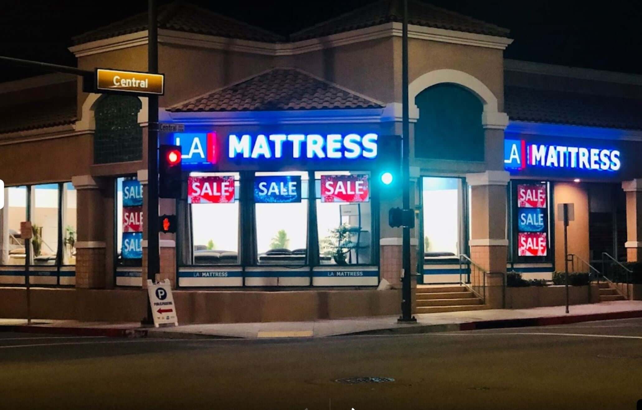 A Mattress store illuminated at night, featuring 'Sale' signs in the windows and a stoplight nearby.