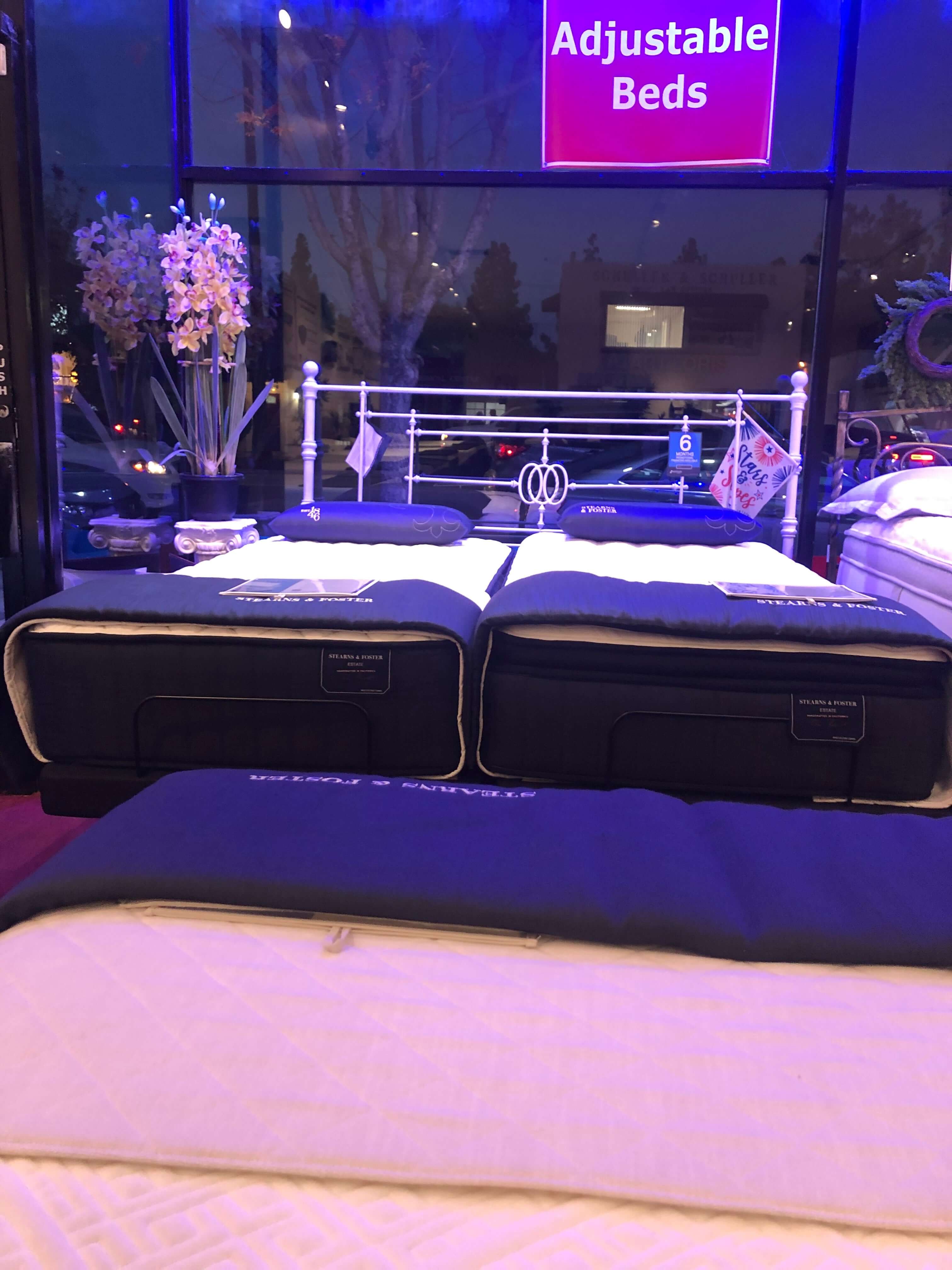 Adjustable beds showcased in a store with colorful lighting and floral arrangements in the background.