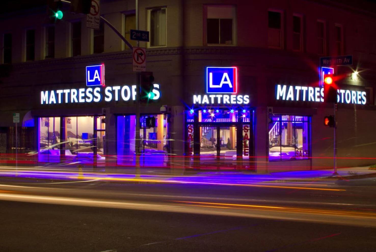 Nighttime view of LA Mattress Stores with bright neon signage and traffic lights, showcasing a modern retail environment.