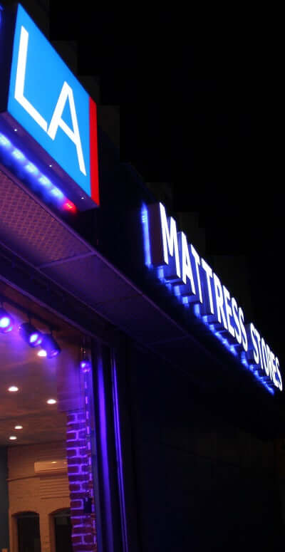 Illuminated sign of LA Mattress Stores at night, showcasing vibrant blue lights and modern design.