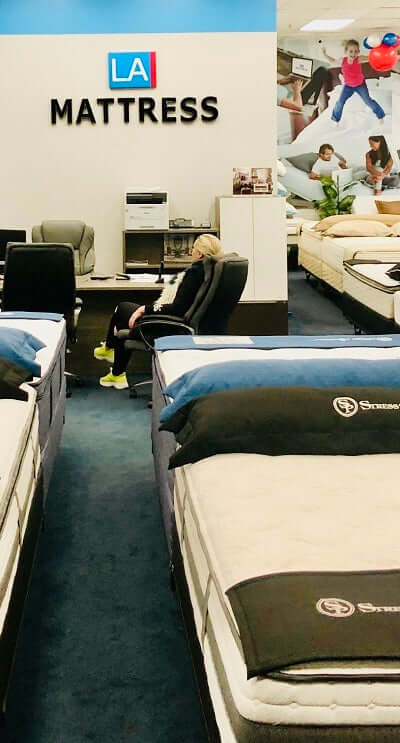 A woman sitting in the LA Mattress store surrounded by various mattress displays, showcasing a cozy shopping environment.