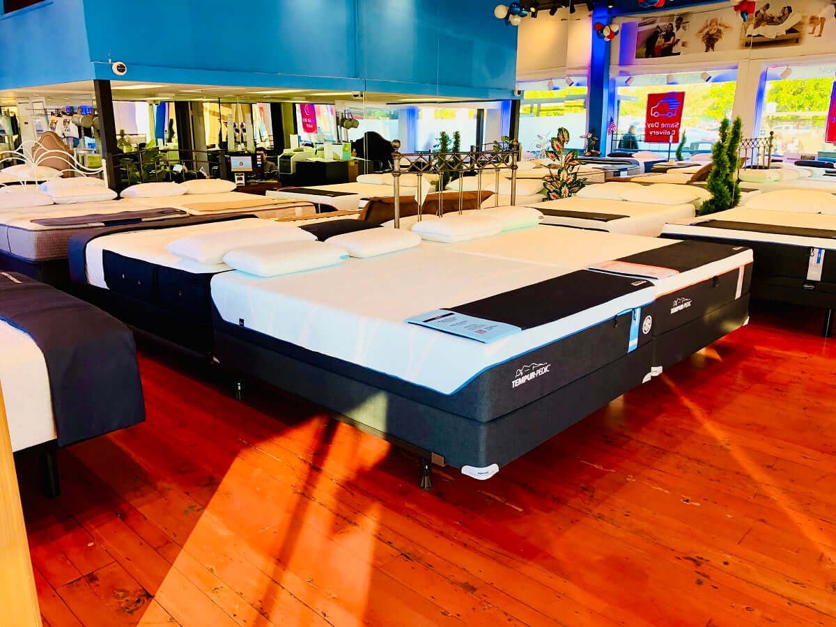 Showroom featuring various mattress displays on a polished wooden floor, highlighting sleep product options.