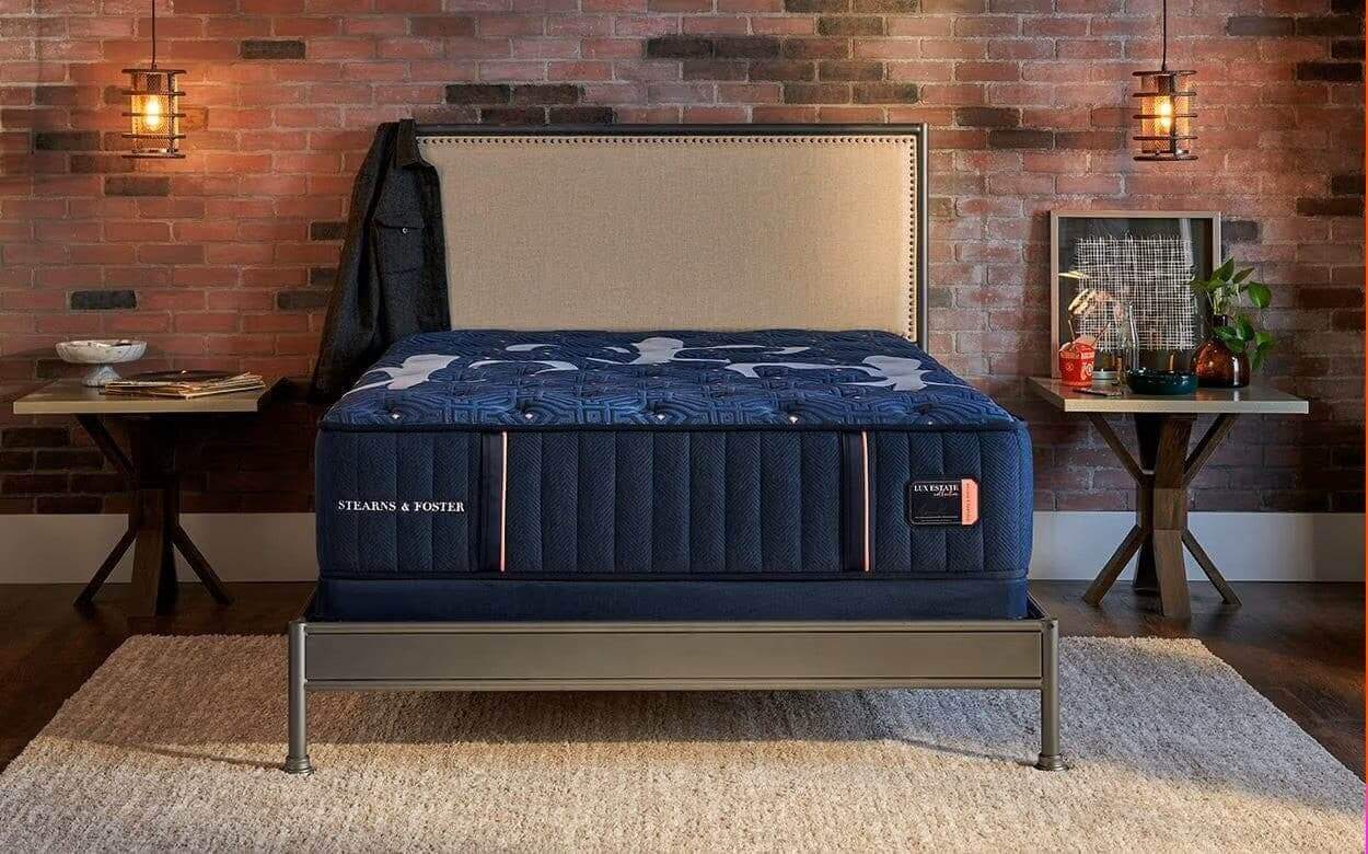 Stearns & Foster Lux Estate Medium 14.5" Mattress displayed in a stylish bedroom setting with rustic brick wall.