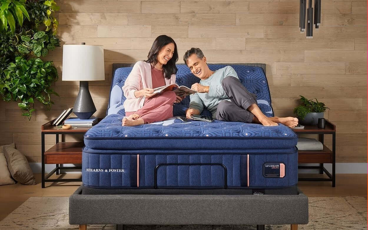 Couple relaxing on a comfortable mattress, enjoying a book together in a cozy bedroom setting.