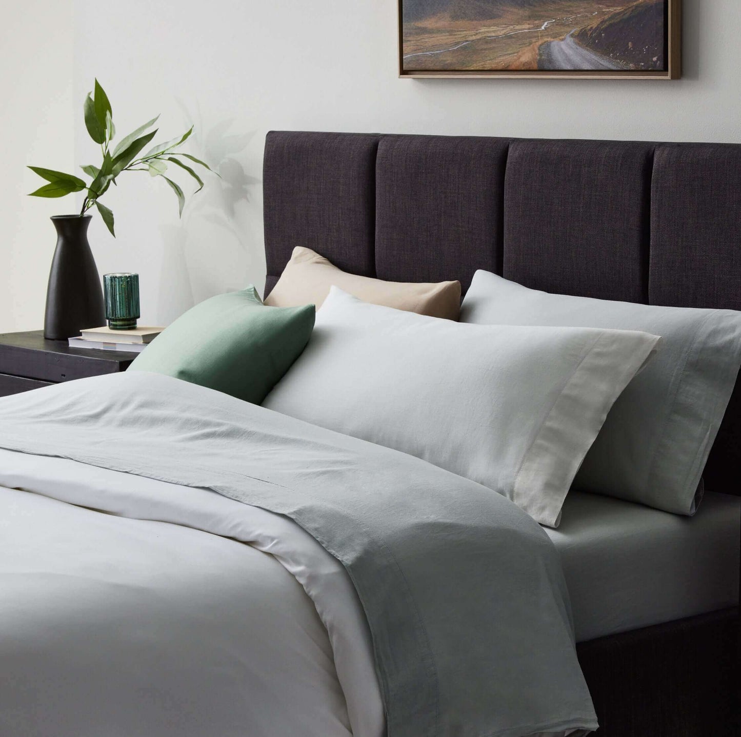 Malouf Fog Linen Weave Cotton Sheet Set displayed on a neatly made bed with soft green and neutral pillows against a dark headboard.