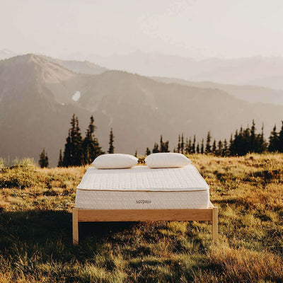 Twin XL Savvy Rest Serenity organic latex mattress on a wooden bed frame in a scenic mountain setting.