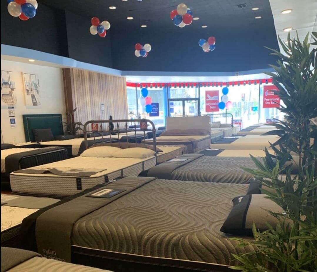 Showroom display of various mattresses with decorated ceiling balloons for promotional event.