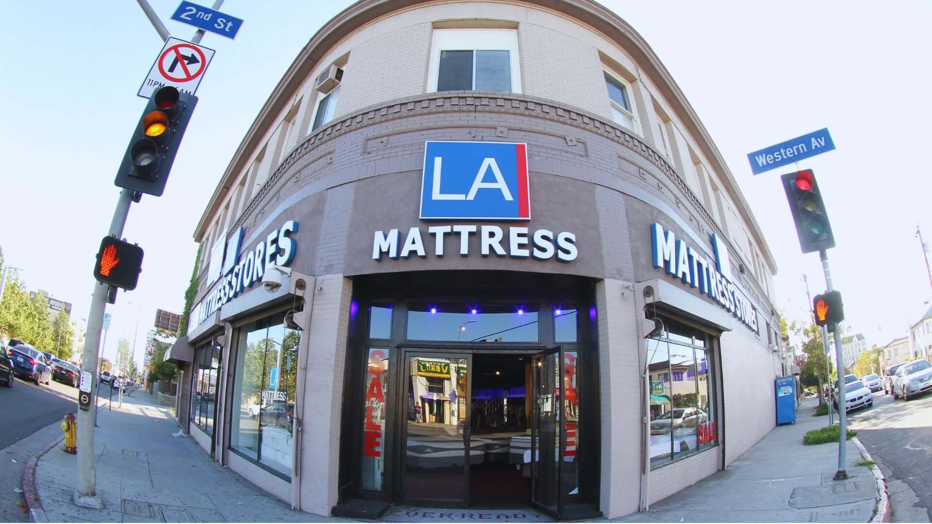 Exterior view of LA Mattress store at the corner of 2nd St and Western Ave, showcasing bright signage and street traffic.