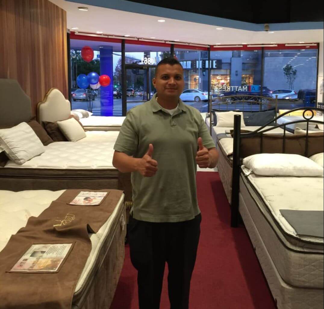 Salesperson giving thumbs up in a mattress showroom with various beds on display.