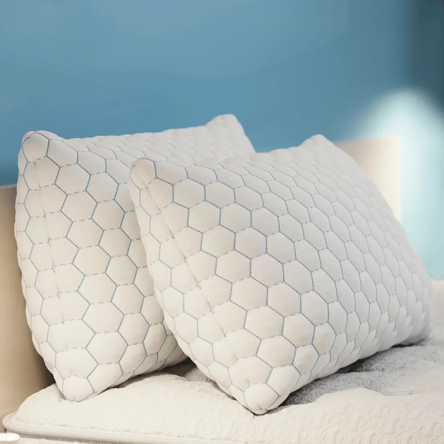 Two cozy white pillows with a honeycomb pattern resting on a bed against a blue wall.