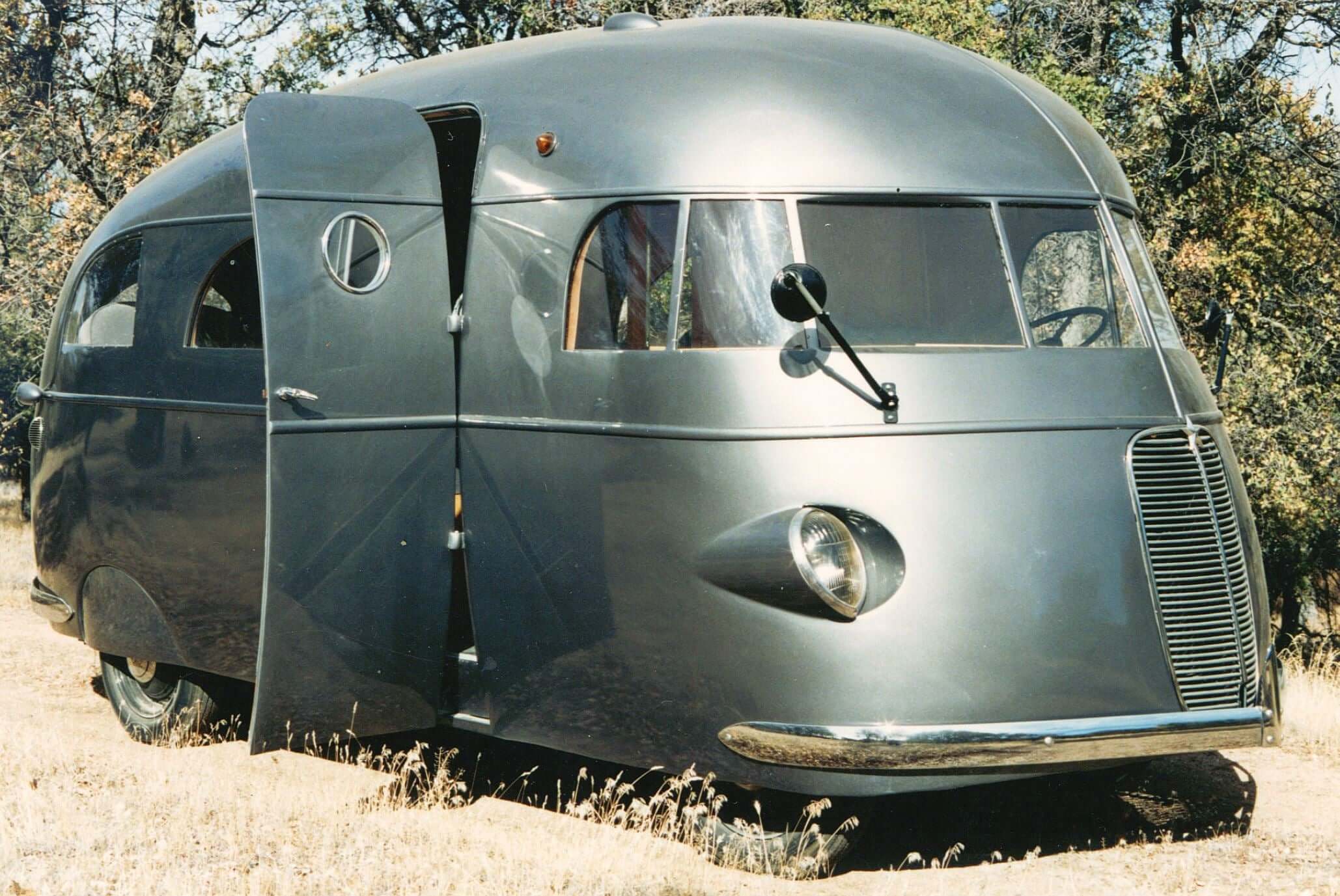 Vintage streamlined metal RV parked in a natural setting, showcasing its unique design and large front door.