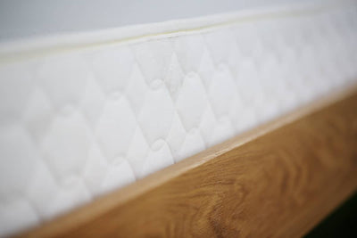 Close-up of Savvy Rest mattress foundation featuring a quilted design and natural wood edge for organic mattress support.