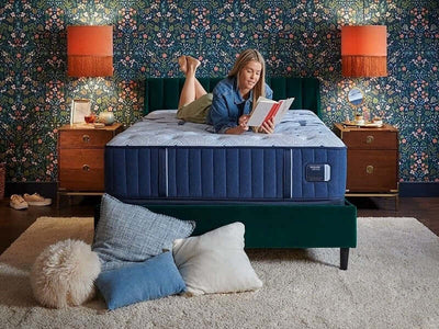 Woman reading on the Stearns & Foster Estate Firm mattress in a cozy, stylish bedroom setting.