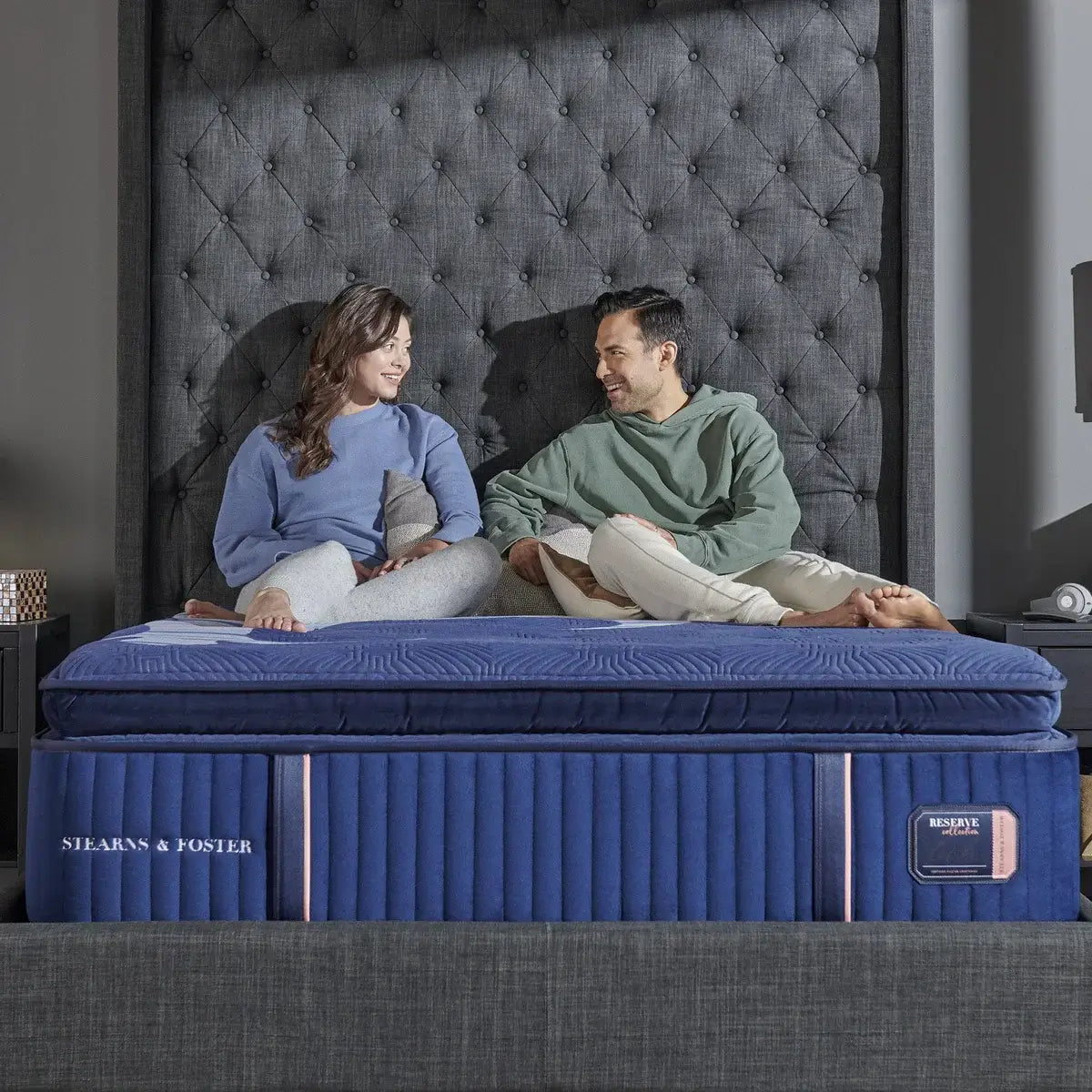 Couple enjoying comfort on a Stearns & Foster mattress in a chic bedroom setting with a tufted headboard.
