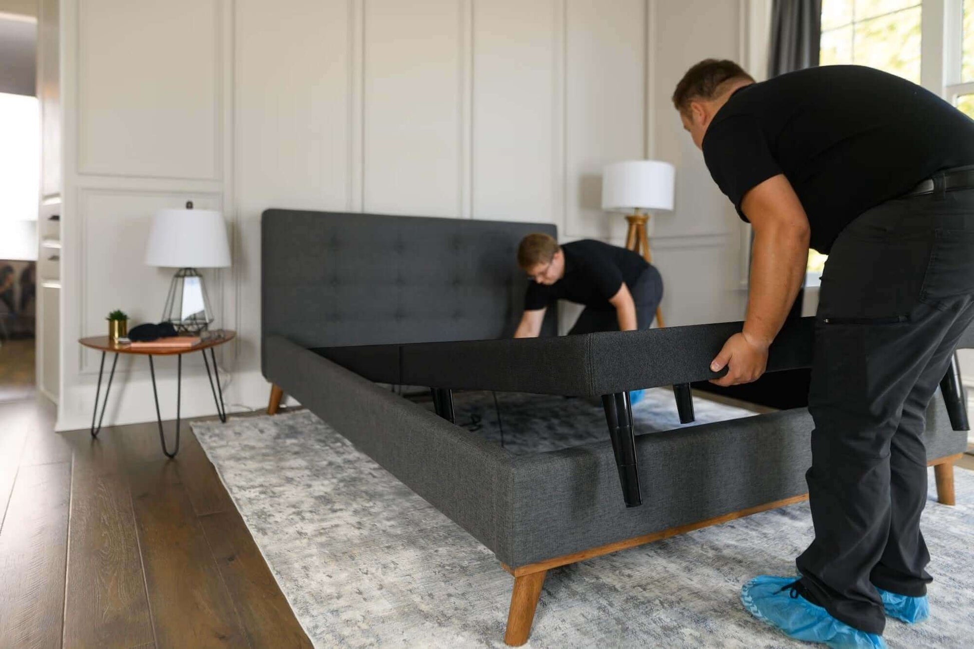 Two men assembling a Tempur-Pedic TEMPUR-Ease™ adjustable base in a modern bedroom setting.