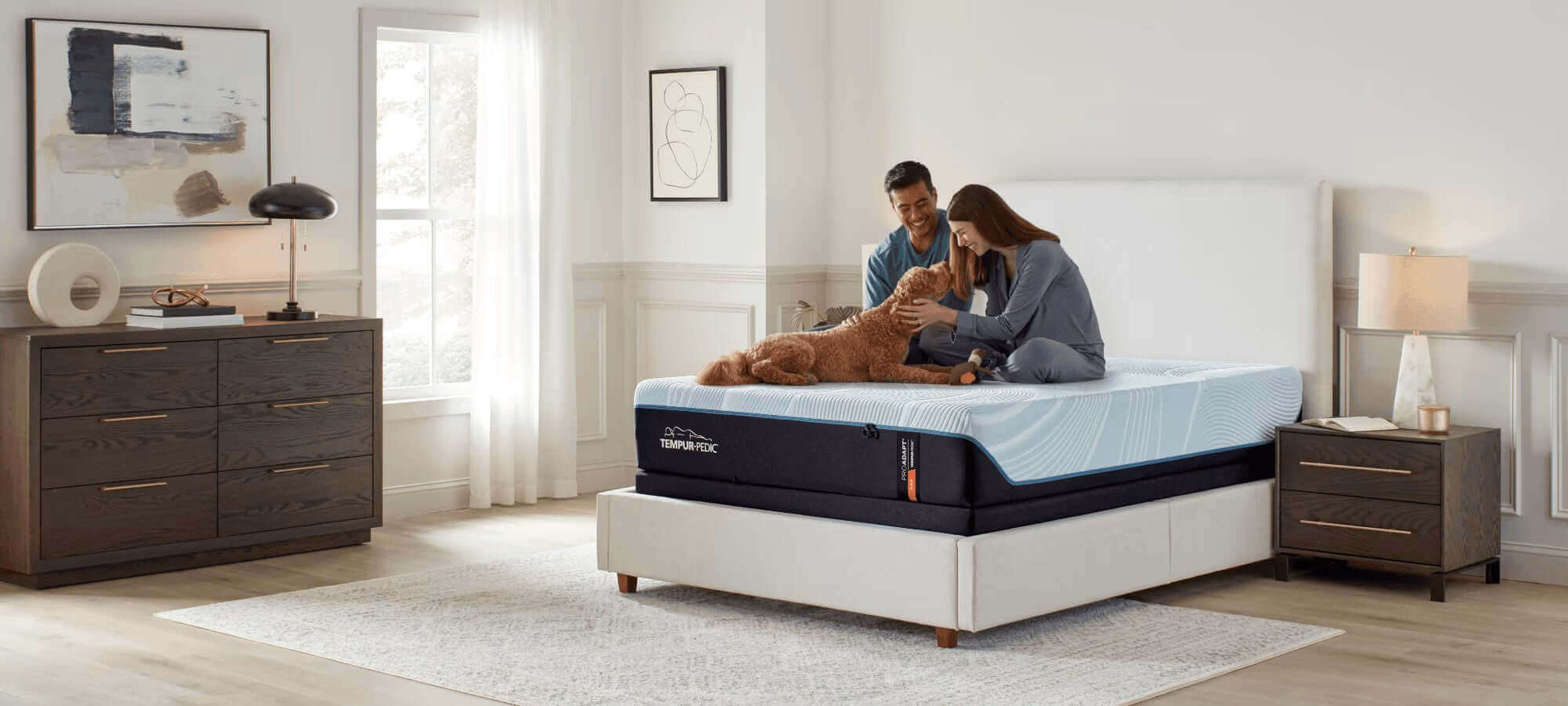 Couple enjoying time with their dog on a Tempur-Pedic TEMPUR-ProAdapt® Firm 12" Mattress in a cozy bedroom setting.