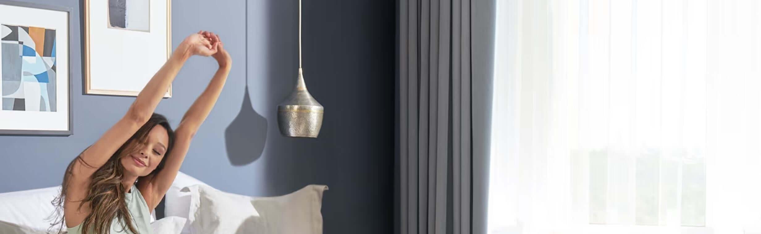 A woman stretching in a cozy bedroom with modern decor and natural light streaming through the window.