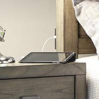Modern bedside scene featuring an iPad charging on a greystone nightstand with a stylish lamp nearby.