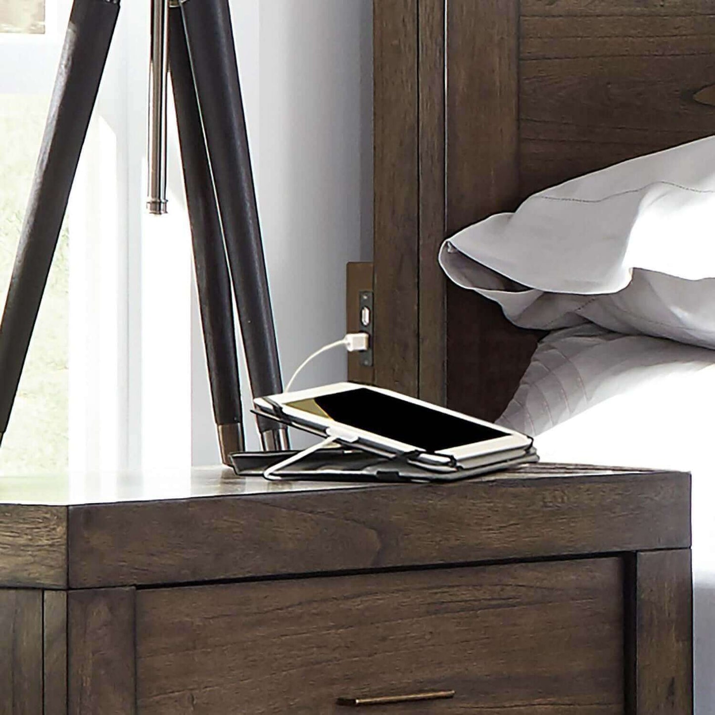 smartphone charging on a stylish nightstand next to a bed with modern decor and Greystone finish panel bed frame.