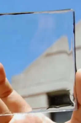 A person holding a clear glass panel against a blue sky, showcasing its transparency and reflection.