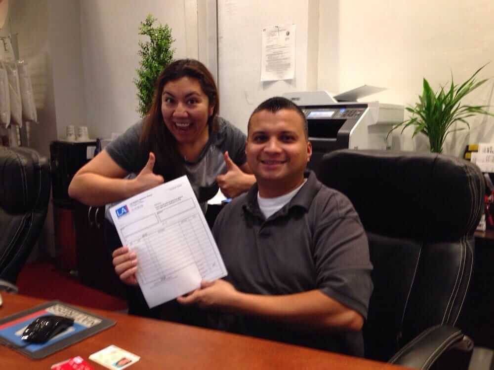 Happy team members giving thumbs up while showing a completed form in an office setting.