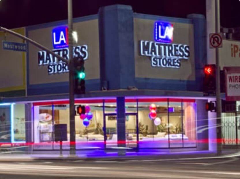 Night view of LA Mattress Stores showcasing vibrant lighting and promotional balloons outside the storefront.