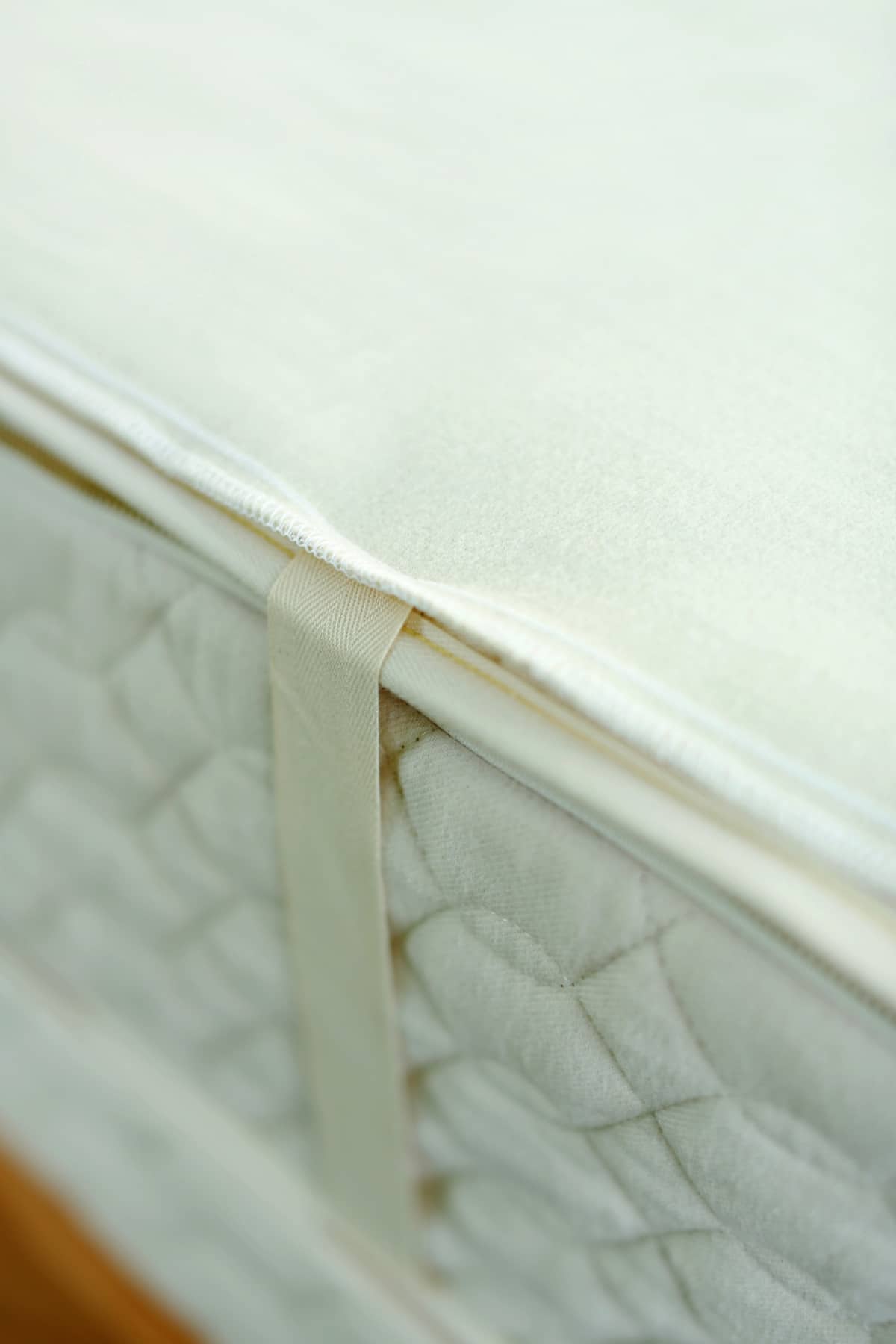Close-up of King Savvy Rest organic wool mattress pad with organic cotton corner ties for secure fit on a mattress.