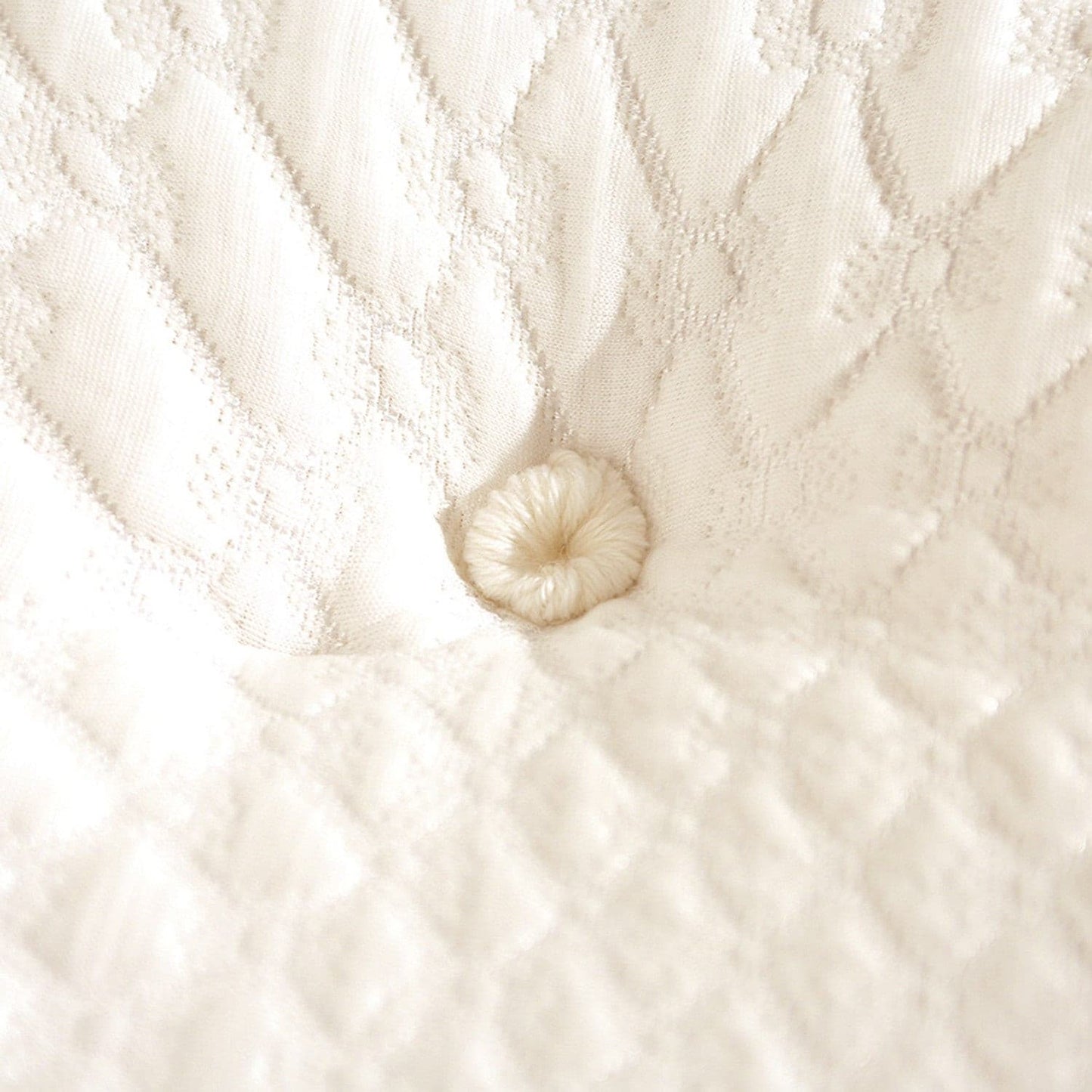 Close-up of a button on a cream-colored mattress fabric with quilted texture.