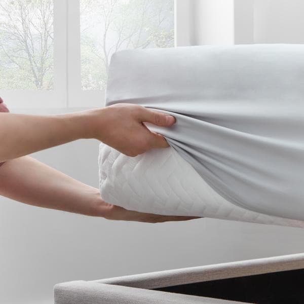 Person adjusting a soft, cozy microfiber sheet set on a mattress for a secure fit and easy care.