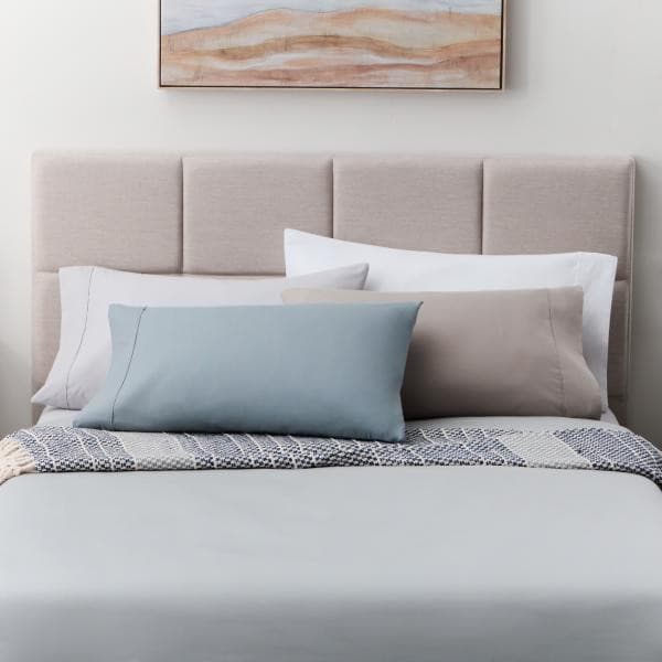 Soft knit microfiber pillowcase set displayed on a bed with neutral and blue accent pillows against a beige headboard.