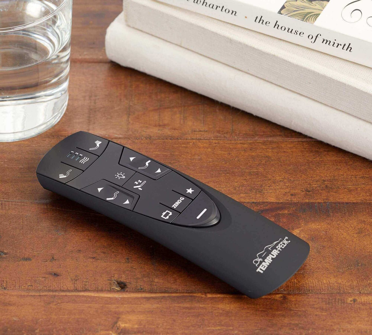 Remote control for Tempur-Pedic TEMPUR-Extend adjustable base on a wooden table next to a glass of water and book.