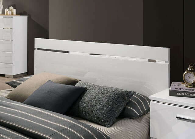 Modern white gloss bed headboard with sleek chrome accents and decorative pillows in a stylish bedroom setting.