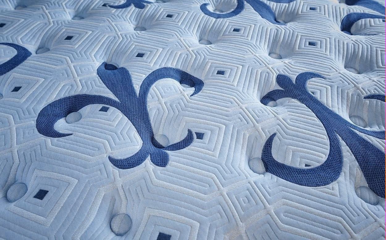 Close-up of a stylish blue mattress pattern with intricate geometric designs and contrasting dark blue swirls.