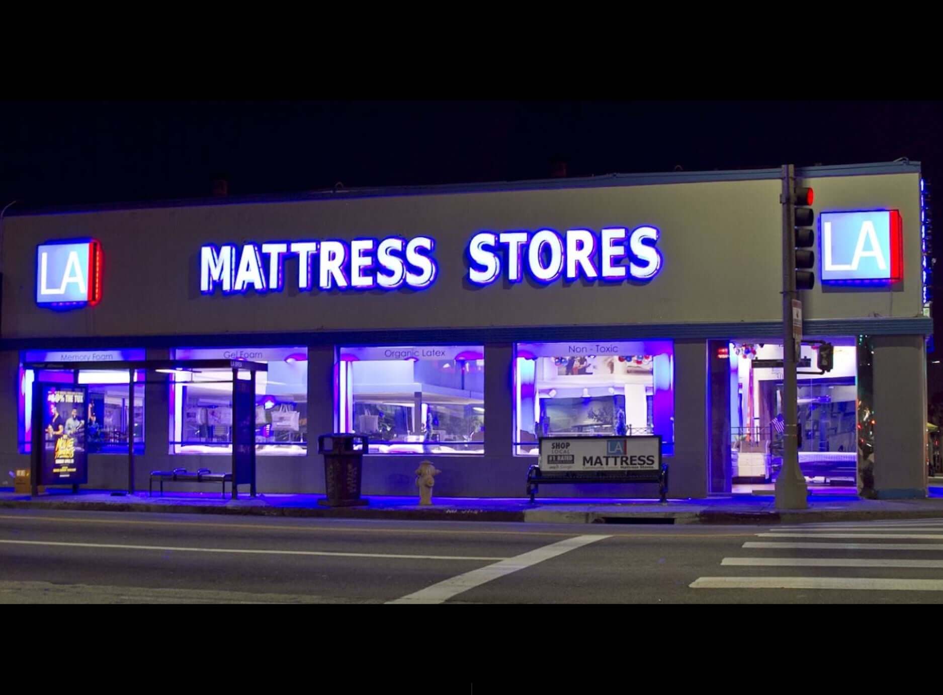 Brightly lit LA Mattress Stores storefront at night, showcasing various mattress displays and signage.