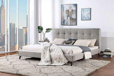 Mid-century modern gray platform bed with tufted headboard in a bright room with city view and cozy decor.