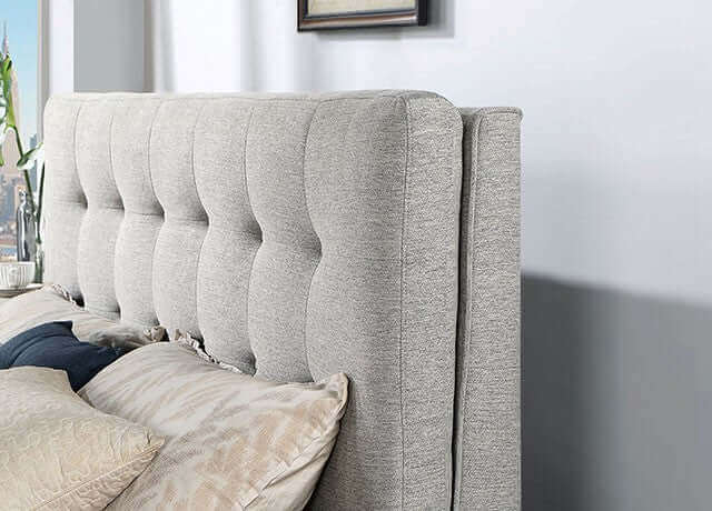 Mid-century modern gray padded headboard with biscuit tufting and plush pillows on the bed.