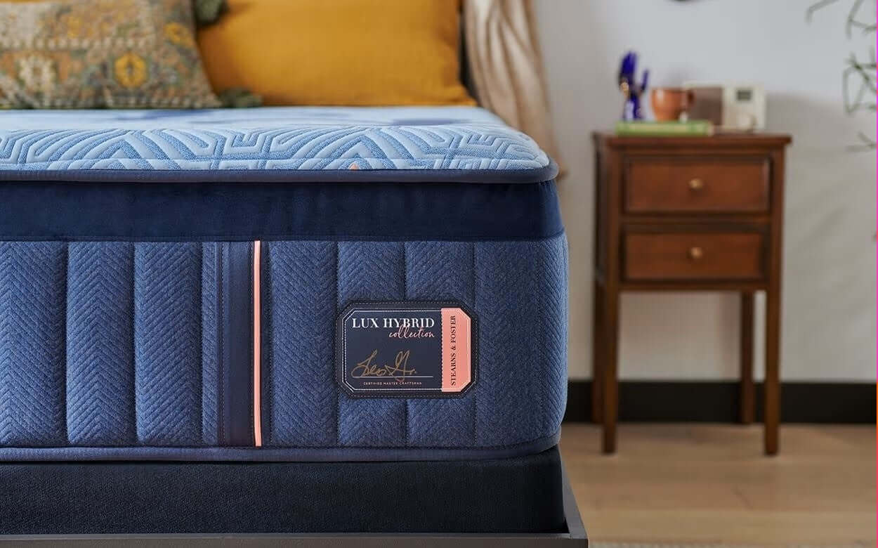 Stearns & Foster Lux Hybrid Plush 14.5" Mattress showcasing blue quilted top and elegant side details in a cozy bedroom setting.
