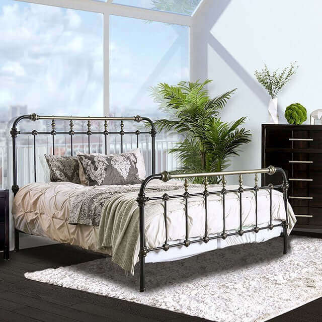Riana Dark Bronze Metal Bed in a bright bedroom with plants, showcasing antique design and decorative accents.