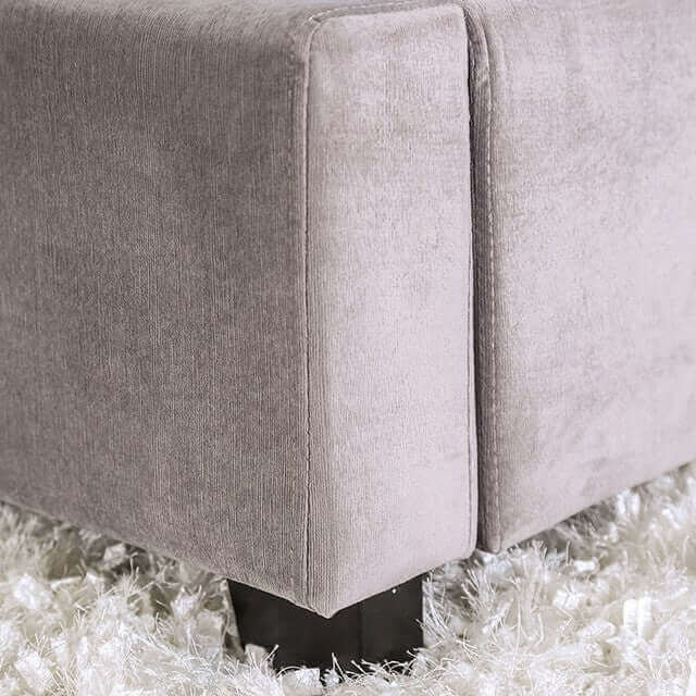 Close-up of a soft, gray tufted bed corner with sleek black legs on a fluffy rug.