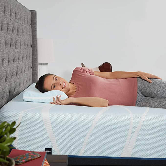Woman using Tempur-Breeze° Neck + Cooling Pillow on a bed, showcasing comfort and support for better sleep quality.