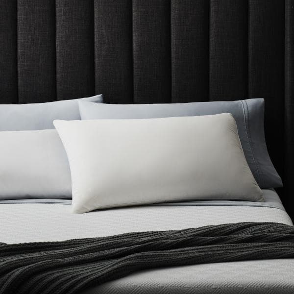Malouf Cotton Encased Down Blend Pillow on a neatly made bed with soft bedding and dark headboard.