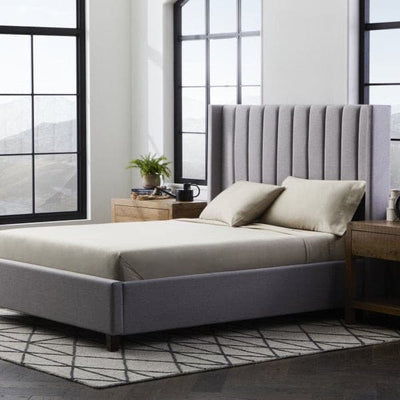 Modern bedroom featuring a gray upholstered bed with Malouf Smooth Driftwood Bamboo Rayon sheets and stylish decor.